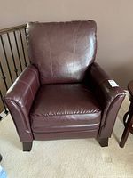 Front view of the maroon leather recliner chair showing full upholstery and wooden legs.