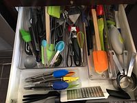Drawer with varied kitchen utensils such as tongs with silicone tips, ladle, whisks, spatulas, cheese grater, and measuring cups