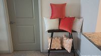 Six assorted throw pillows displayed on and under a chair against a wall with a door and granite countertop visible.
