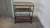 Wood and metal bar cart with three wooden shelves and caster wheels