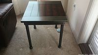 Side view of one mahogany colored wood and metal end table showing metal legs and wood top.