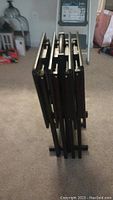 Photo of the set of four coffee tables shown in a folded, stacked position, revealing dark tabletops and black folding metal legs.
