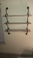 Photo of the wood and metal hanging shelf mounted on a wall showing three wooden shelves and black metal frame supports.