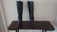 Front view of black knee-high leather boots on table.