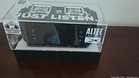 Image of Altec Lansing speaker inside transparent plastic box showing wirelessly charging station and speaker controls on front panel.