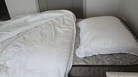 Two white twin comforters and two matching pillow shams, laid out on twin mattress.