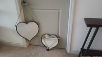 Photo showing two heart-shaped hanging wall mirrors placed against a door, one larger and one smaller, both with hanging ropes attached.