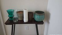 Six assorted vases and planters on a dark wood shelf against a light wall backdrop.