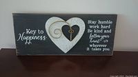 Front view of wood wall plaque showing two interlocked white hearts with a key design and printed inspirational quote in white text on a dark wood background.
