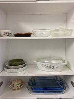 Three shelves showing assorted glass and ceramic bakeware dishes including Pyrex pans and casserole dishes