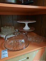 Overview of all glass cake stands, dome, and serving plates on a shelf, showing the various shapes and styles.