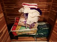 Stack of hand-knitted throws, wool blankets, and duvets in storage bags captured inside a wooden room.