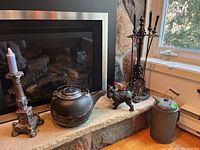 Photo showing metal cowbell with wooden handle and set of black fireplace tools on stand by fireplace.