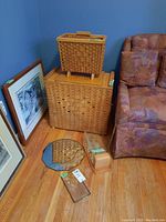 Photo of wicker magazine rack, wicker laundry hamper, small wooden box, small framed mirror, and a portion of a patterned sofa.
