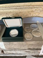 Photo of Calgary 1988 $20 Olympic coin in green velvet presentation case and original box beside four Montreal 1976 Olympic silver coins in capsules.