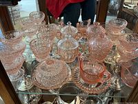 Shelf with an assortment of pink glassware including pedestal bowls, covered candy dish, cream and sugar bowls, and other small dishes