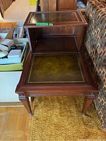 Close-up view of one two-tier side table showing detailed embossed leather inlay on top surface and open middle shelf with caster wheels on legs.