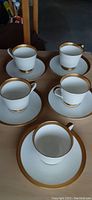 Five fine bone china cups and saucers with gold rims arranged on a surface, viewed from above.