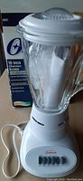 Oster 10-speed blender with glass jar and original box in background, white base with buttons, heavy glass pitcher with lid, blender cord visible.