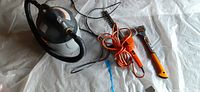 Three garden tools placed on the ground covered with plastic: wet/dry shop vacuum on left, orange corded hedge trimmer in middle, small leaf blower/vacuum on right.