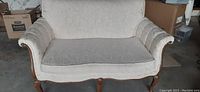 Front view of white antique loveseat with floral patterned fabric and wood legs