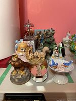 Wide view of multiple animal figurines and music boxes on tabletop including eagle, squirrels, dog, penguins, and blue birds