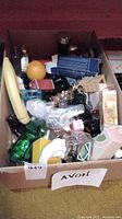 Box containing various Avon collectible glass bottles in unique shapes and colors with original packaging boxes.