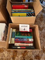 Top view of a box showing a variety of books stacked horizontally and vertically, with a handwritten 'FICTION' label.