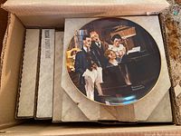 Photo of one Knowles collector plate featuring a Norman Rockwell painting, displayed on top of a box with other boxed plates visible underneath.