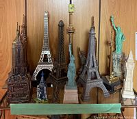 Front view of miniature building collection on a wooden shelf showing Empire State, Eiffel Tower, Statue of Liberty, Big Ben, and others.