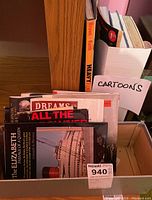 Box holding assorted book covers, a hardcover book, and papers labeled 'Cartoons'