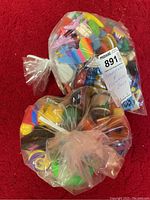 Two sealed plastic bags filled with assorted colorful pencil sharpeners and small figurines on a red carpet.