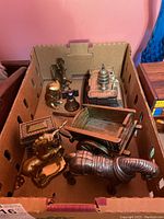 Overview of multiple metal figures in a box including buildings, cart, bell, eagle figure, and horse figure.