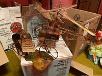 Bicycle and helicopter music boxes shown on top of cardboard boxes, with the bicycle featuring a vintage Americana music box side and skeletal metal frame helicopter above it.