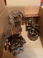 Set of four metal music box sculptures displayed inside a cardboard box, including Ferris wheel, waterwheel mill, carousel, and clown figure.