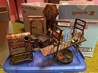 Image of metal sculptures placed on a blue plastic container, showing multiple small metal objects including a suspension bridge, a building facade, and luggage items.