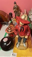 Overview of four items on a patterned surface including cowboy figurine, lantern, pipe-smoking man figurine, and award ball.