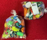 Two clear plastic bags filled with numerous colorful and novelty pencil sharpeners on a red carpet.