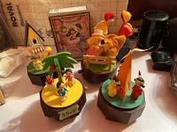 Five vintage painted wood and plastic music boxes arranged together showing whimsical figures such as pirates, dancers, and a clown with tent, on round and octagonal bases.