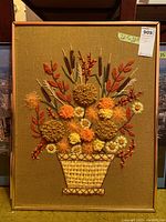 Full view of the framed fabric art depicting a woven basket with various textured autumn flowers and stems on a brown fabric background.