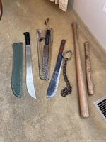 Full lot arranged on carpet showing two wooden bats, three machetes in various conditions, and heavy chain with handle.