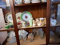 Wide view of wooden shelf displaying various china tea cups, saucers, decorative plates, glassware, and vases.