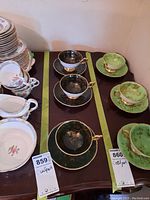 Wide view of multiple teacups and saucers including dark green and light green Coalport sets on a dark wood table.