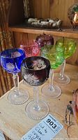 Six colored cut to clear crystal glasses arranged in two rows, showing full set and mixture of colors, starburst cut designs visible.