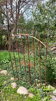 Full view of the iron garden gate set in a natural outdoor environment showing height and rusted finish.