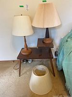 Pair of turned wood lamps on dark wooden multi-level table, plus an extra cream pleated lampshade on floor in front