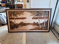 Full view of framed landscape painting showing trees, water and distant land in earth tones