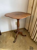 Full view of wooden pedestal table showing scalloped edges and turned base, visible scratches on top.