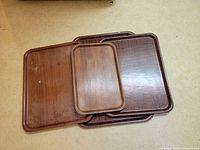 Four simulated teak wood serving trays stacked and angled to show different sizes and wood grain finish.