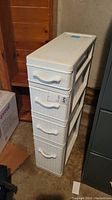 Front and side angle view of the white plastic utility organizer with four drawers showing textured drawer faces and handles.